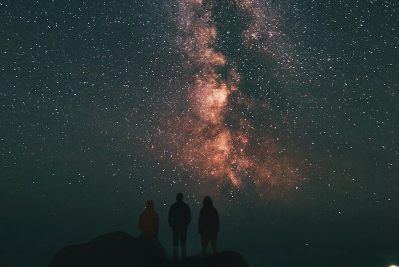 three person looking stars and milky way